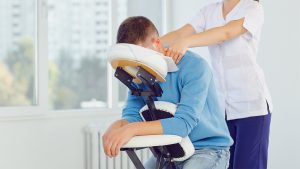 Massage on the massage chair in the office. Masseur does massage to a man sitting on a massage chair in a clinic.