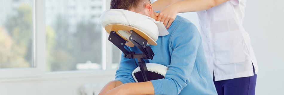 Massage on the massage chair in the office. Masseur does massage to a man sitting on a massage chair in a clinic.